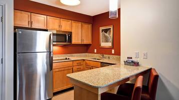 A compact kitchen with wooden cabinets, a stainless steel refrigerator, a microwave, and a granite countertop.
