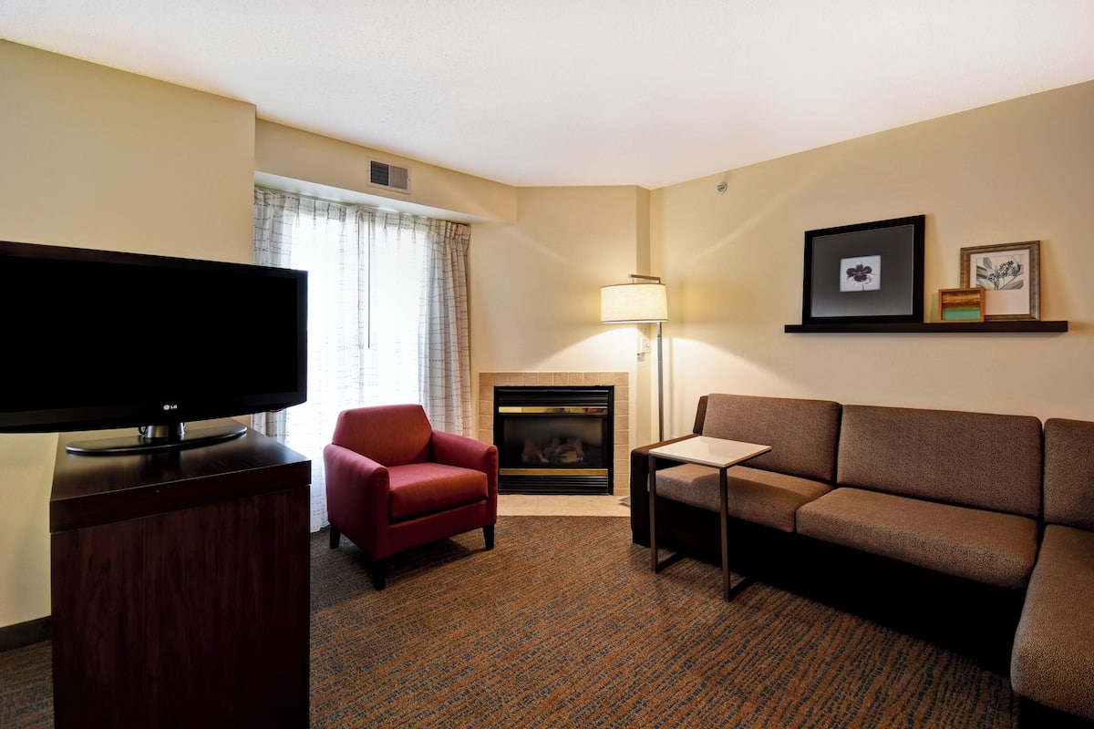 A hotel room with a flat-screen TV, a red armchair, a brown sofa, a fireplace, and a lamp.