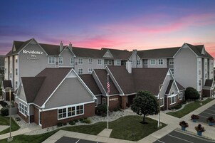 A multi-story hotel with a prominent 'Residence Inn' sign, featuring a mix of brick and siding exteriors, and a parking lot in the foreground.