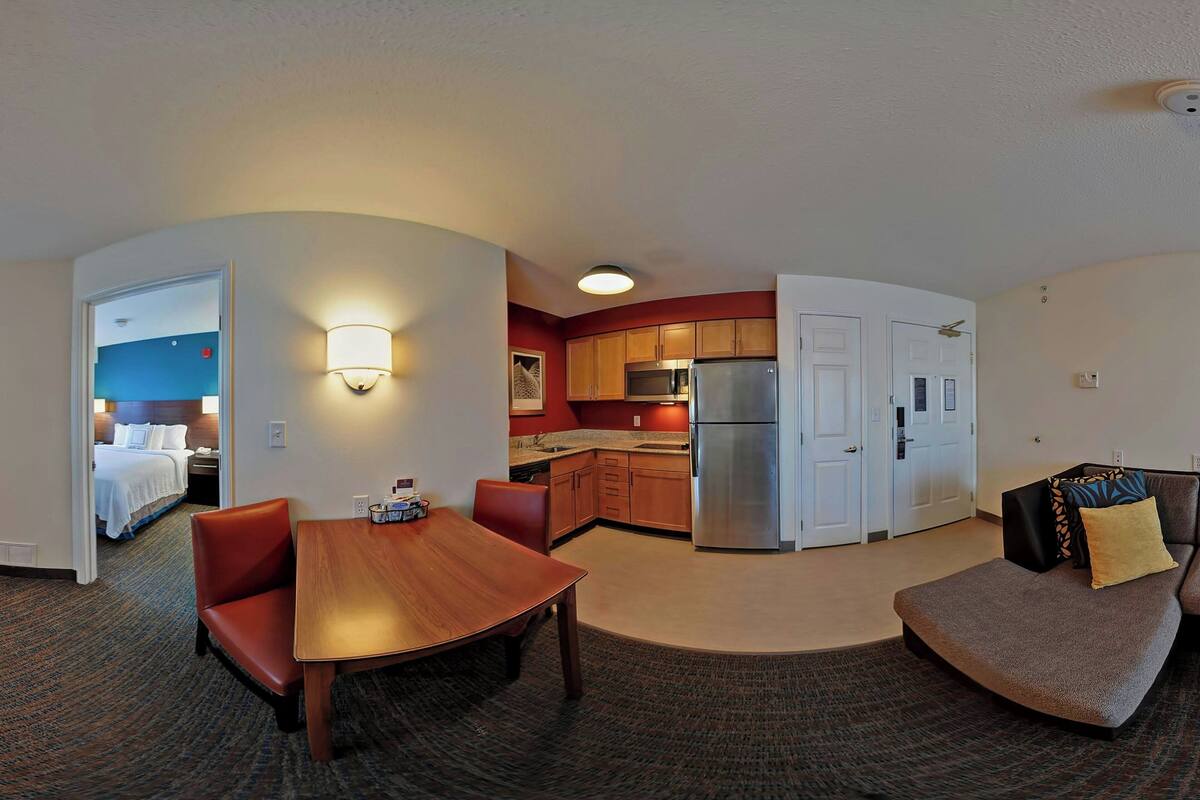 A hotel room with a dining area, kitchenette, and a living area with a sofa.