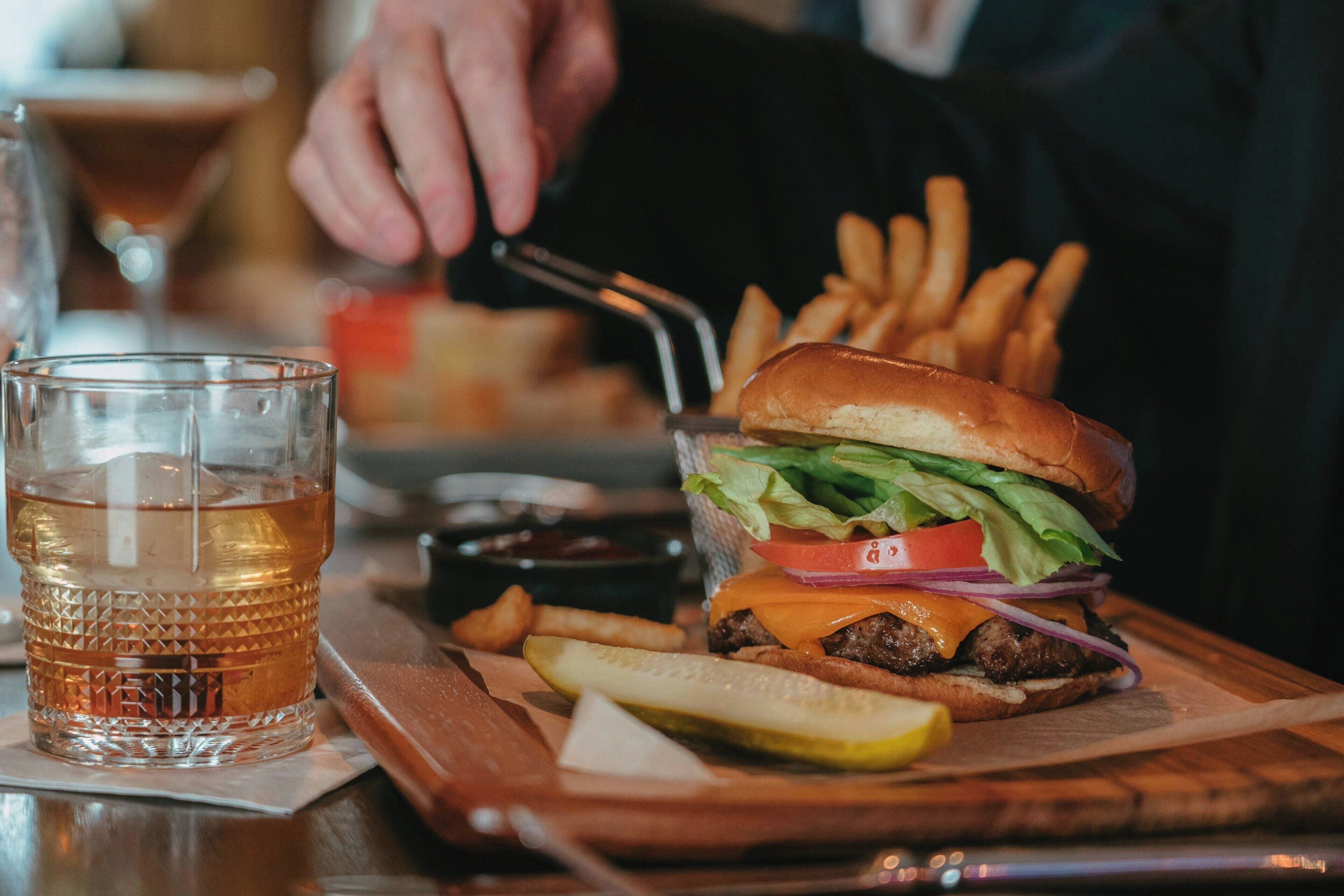A meal consisting of a burger, fries, a pickle, and a drink on a wooden table.