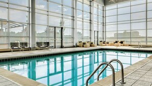 A large indoor swimming pool with clear glass walls, lounge chairs, and a tiled deck area. - Sheraton Overland Park Hotel at the Convention Center (Overland Park)