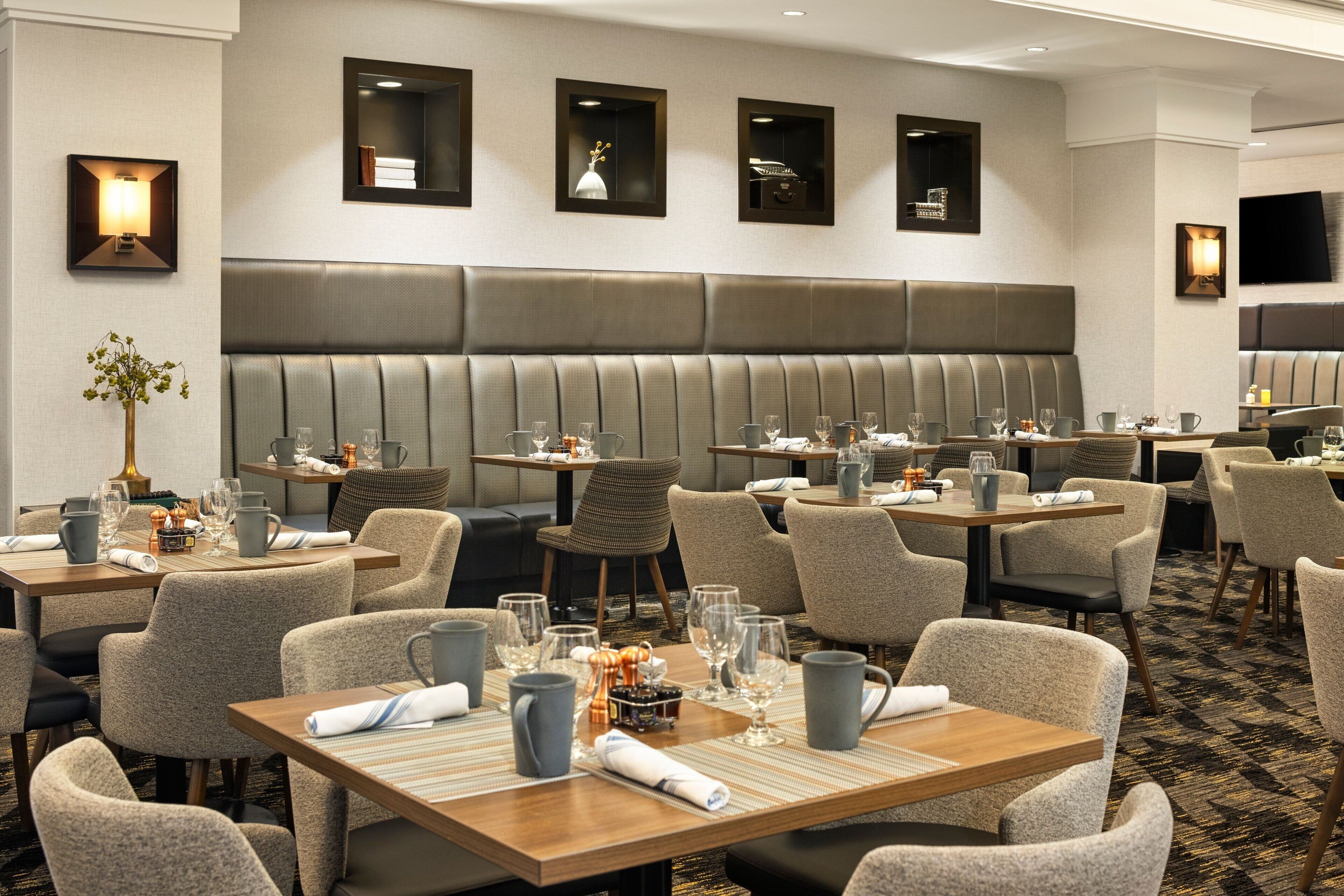 Ein Hotelrestaurant mit mehreren Tischen und Sitzgelegenheiten, ausgestattet mit Gläsern, Besteck und Servietten.