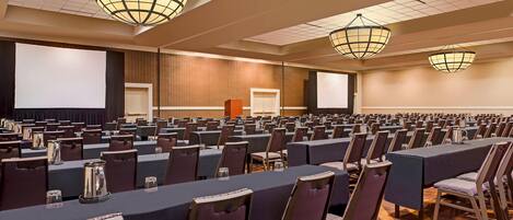 A conference room with rows of tables and chairs, a large screen, and a podium.