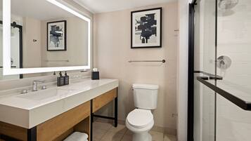 A modern bathroom with a white sink, wooden vanity, a toilet, and a glass shower enclosure.