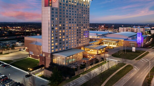 A large hotel with a prominent red logo on the corner building, multiple parking lots, and a well-lit entrance area. - Sheraton Overland Park Hotel at the Convention Center (Overland Park)