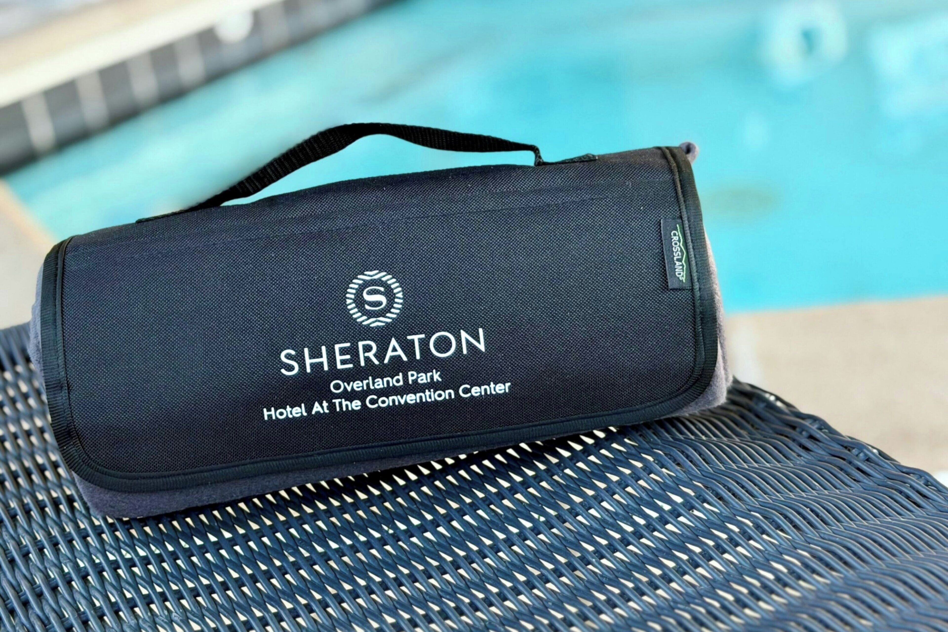 A black Sheraton-branded bag with a handle, placed on a woven chair by a pool.