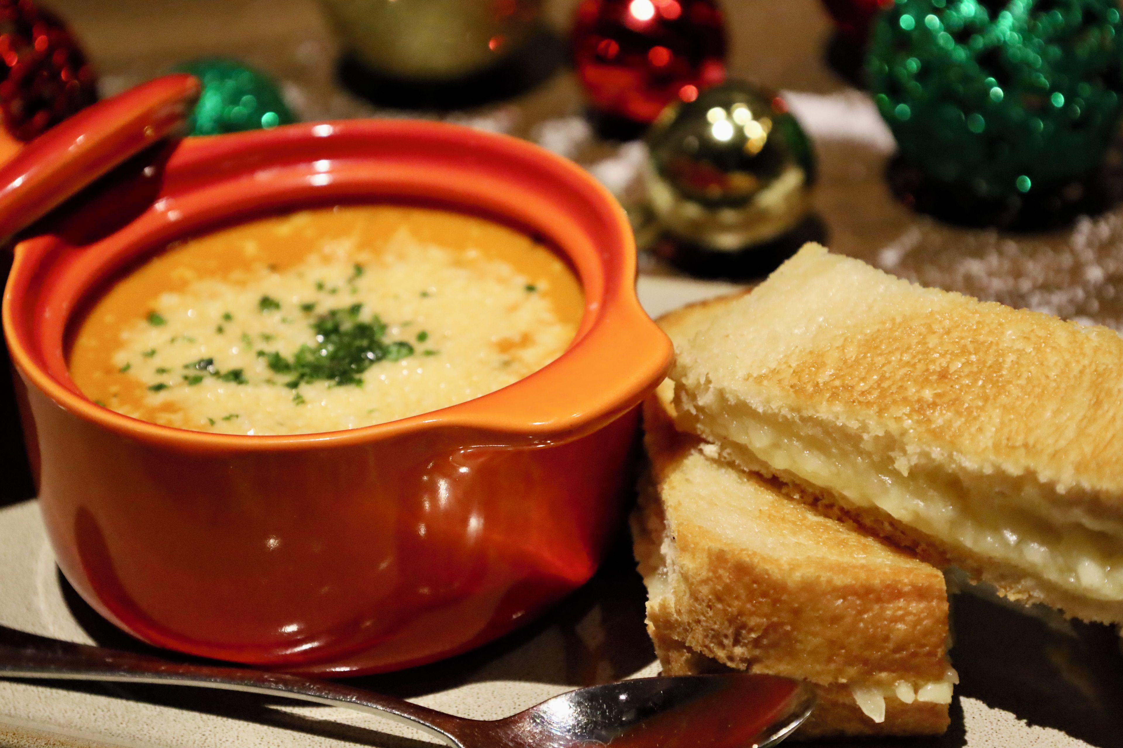 Un tazón de sopa con tapa, acompañado de un sándwich y una cuchara sobre una mesa.