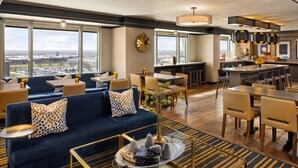 A modern hotel lobby with a large seating area, a bar, and a kitchen visible through the windows. - Sheraton Overland Park Hotel at the Convention Center (Overland Park)
