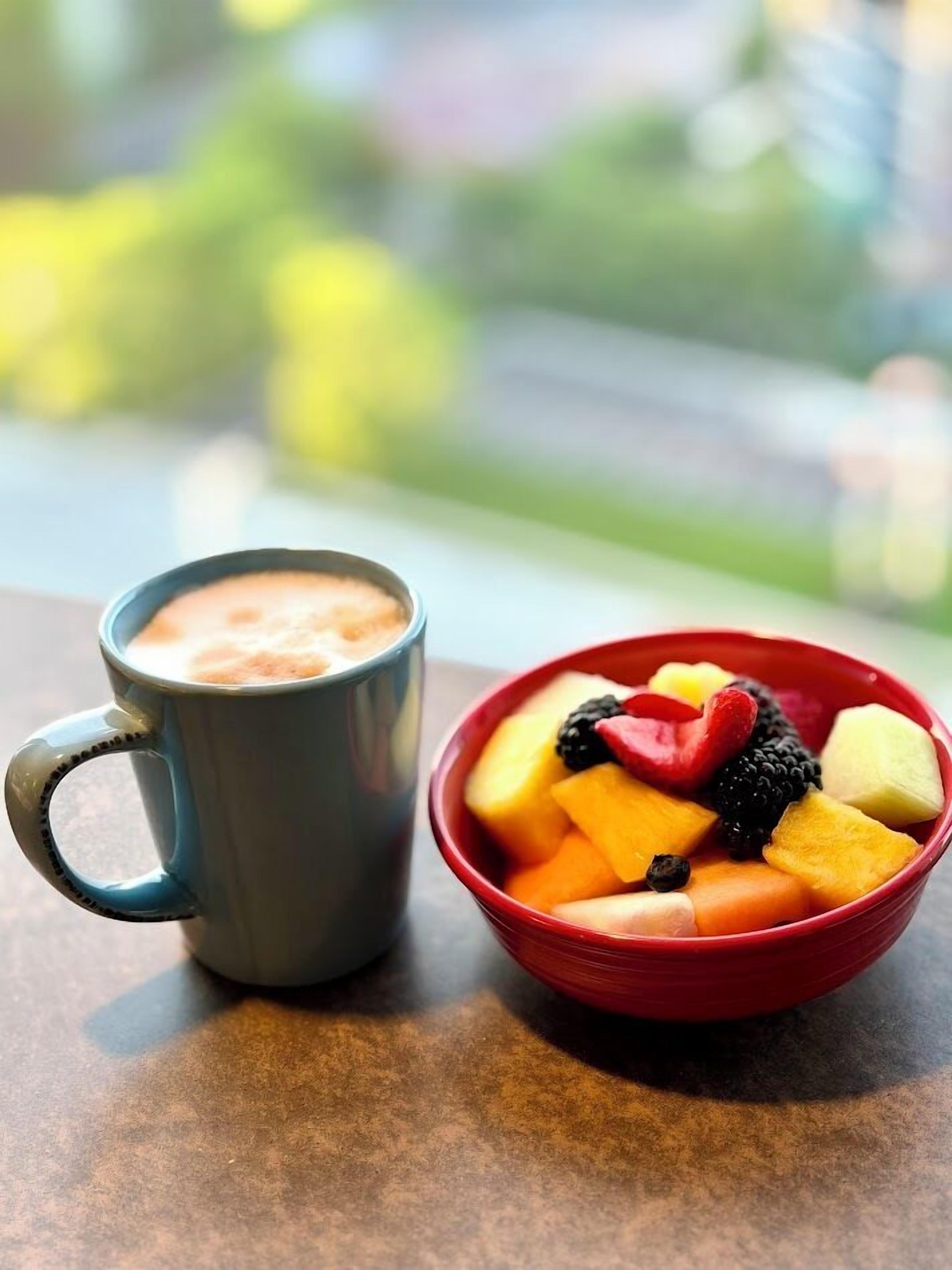 A mug of coffee and a bowl of fruit on a table.