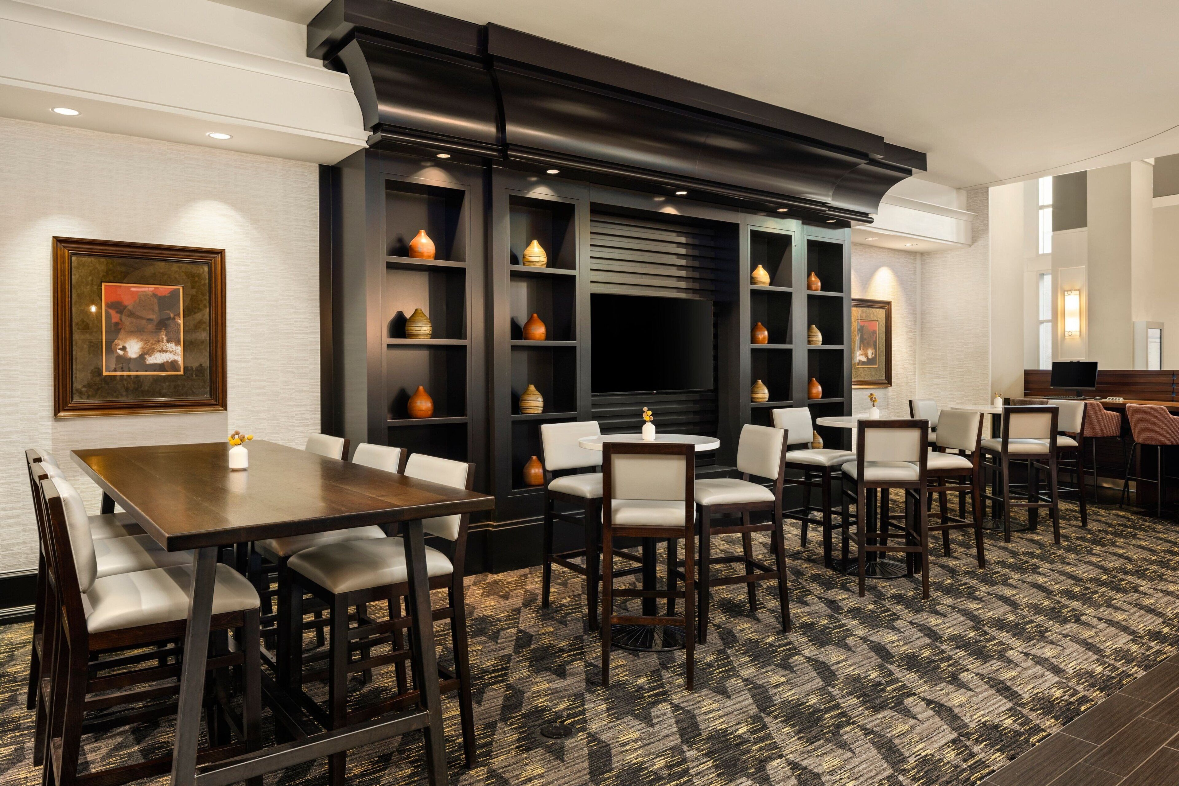 Un comedor de hotel con varias mesas y sillas, una pantalla de televisión grande y jarrones decorativos en estantes.