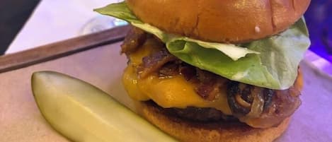 A burger with a pickle on the side, a glass of red wine, and a bar in the background.