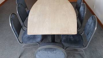 Un salón de conferencias con una mesa rectangular, ocho sillas tapizadas, un cesto de basura pequeño y una puerta de madera.
