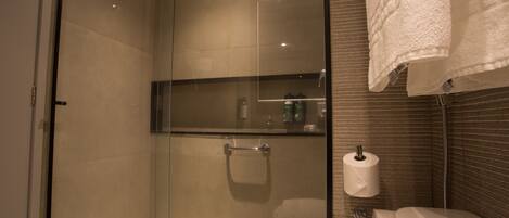 A modern bathroom with a glass shower enclosure, a toilet with a paper towel holder, and a towel rack.