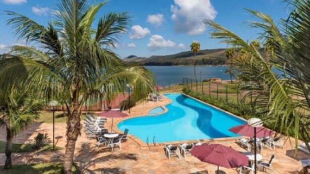 Una piscina de diseño sinuoso, rodeada de palmeras y sillas de descanso, con vistas a un lago y colinas al fondo.