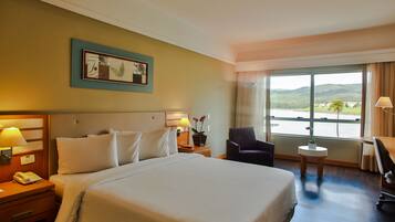 Habitación de hotel con una cama grande, un escritorio, una silla, una mesita y una ventana con vistas al exterior.