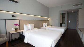 A modern hotel room with two beds, a small table with a potted plant, and a chair.