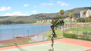 Una cancha de tenis con vista a un lago y colinas al fondo.