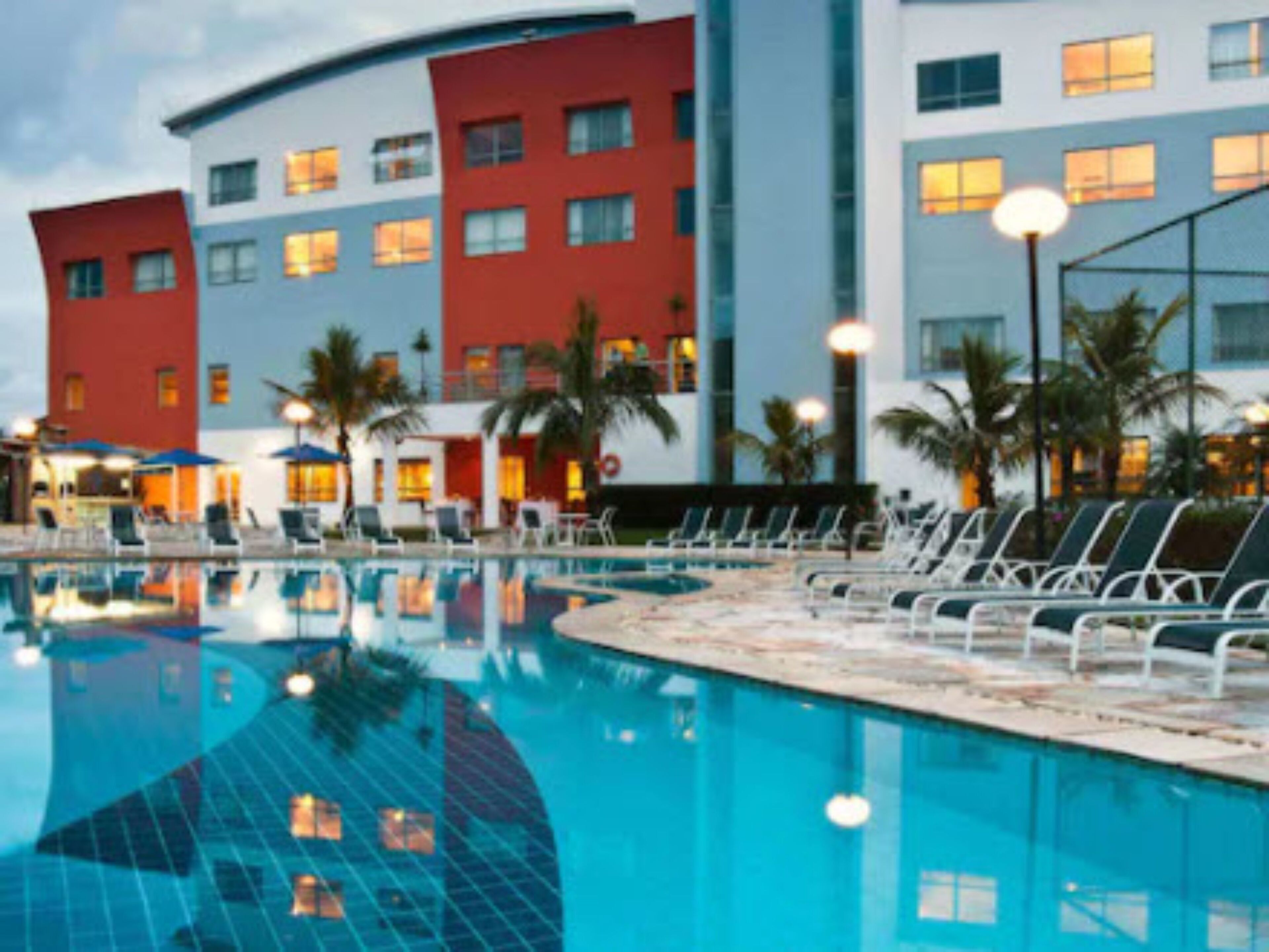 A hotel with a swimming pool, lounge chairs, and palm trees.