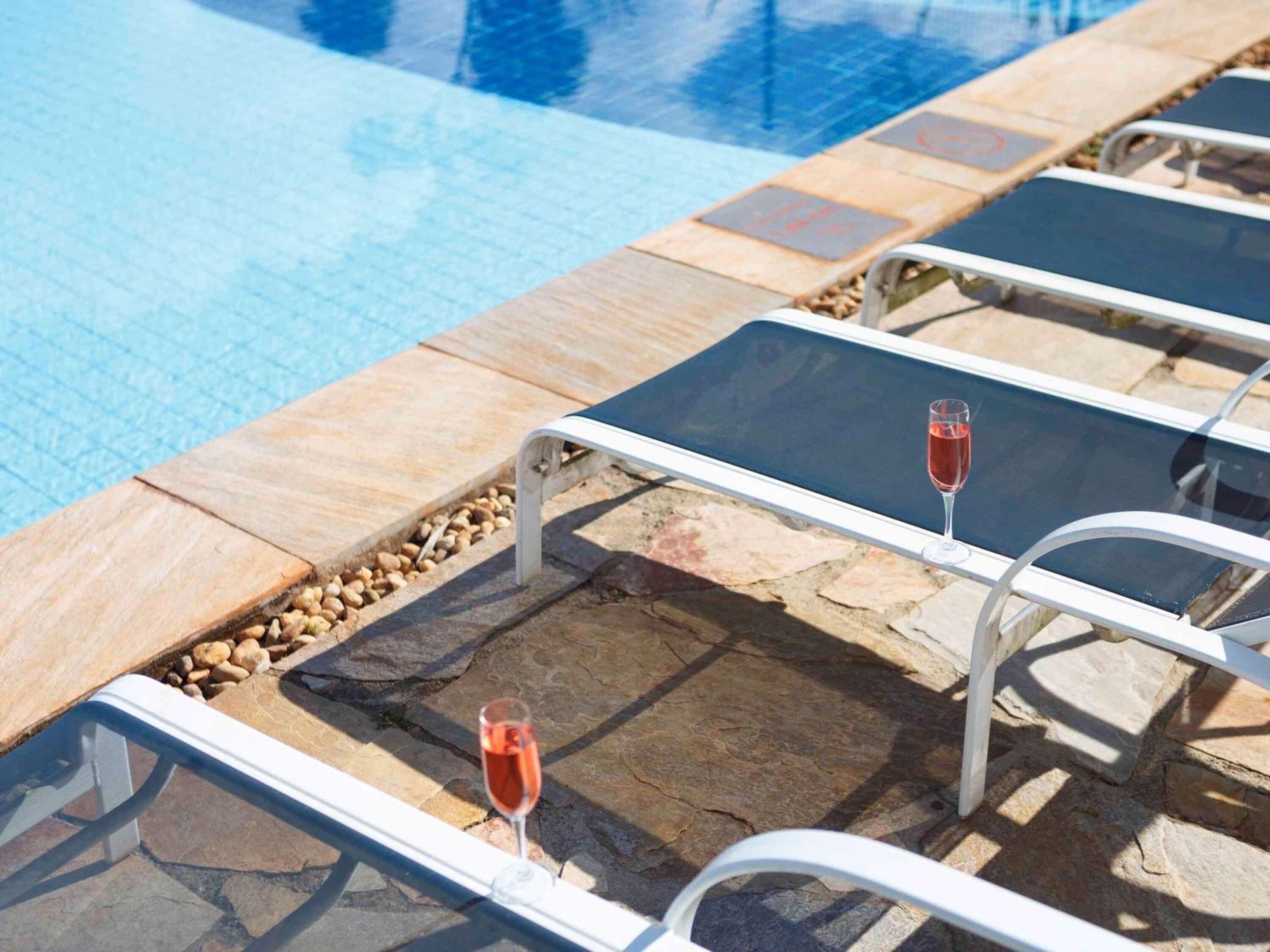 Un área junto a la piscina con sillones de descanso y una copa de vino tinto en cada uno.
