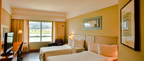 A hotel room with two beds, a desk with a TV, and a view of the outdoors.