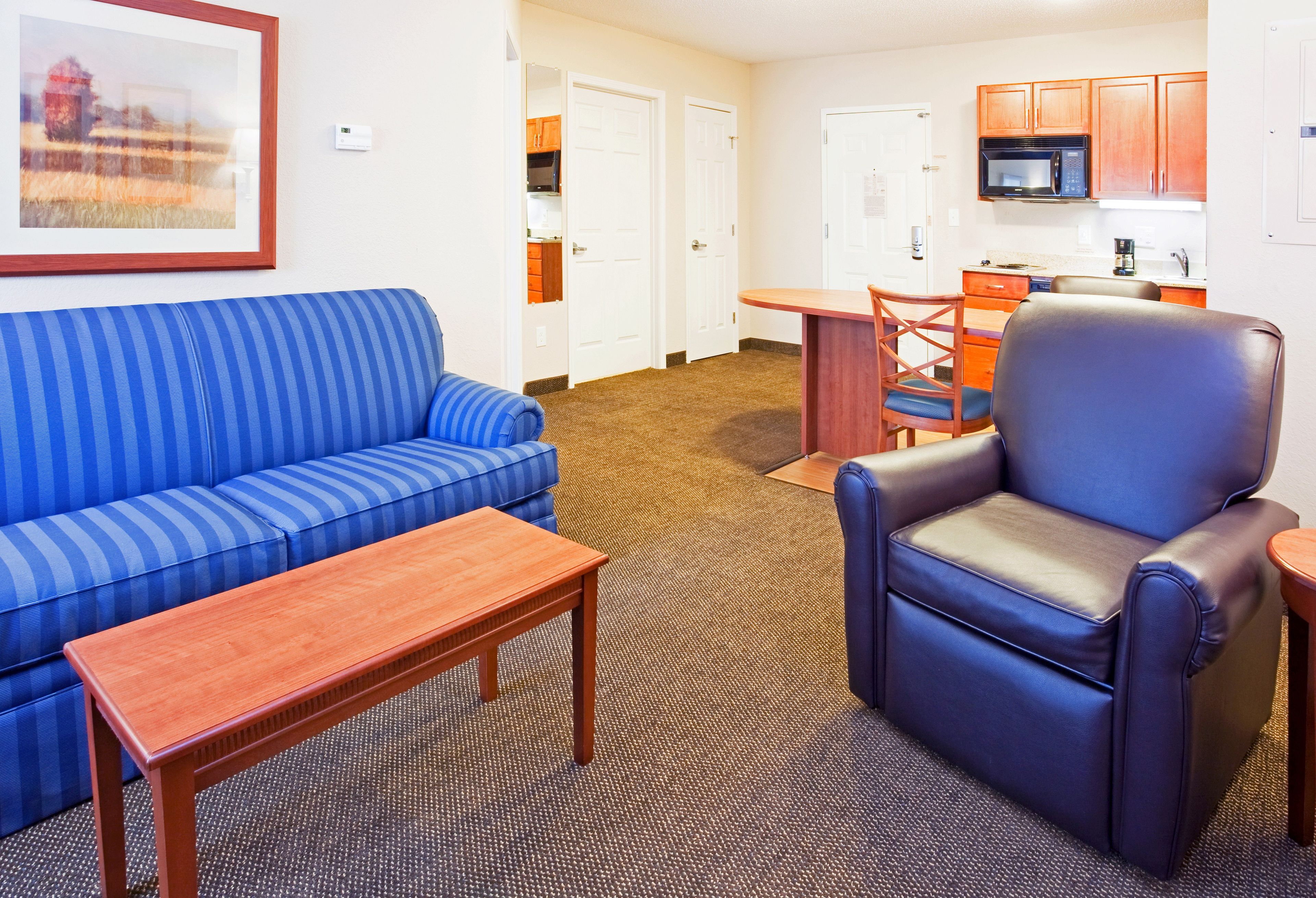 Habitación de hotel con sofá a rayas azules, un sillón de cuero, una mesa de centro de madera y una pequeña mesa de comedor con sillas.