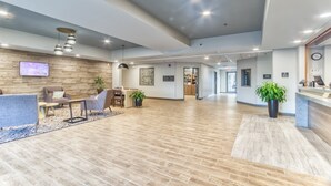 A spacious lobby with a wooden floor, seating area with sofas and chairs, a reception desk, and potted plants.