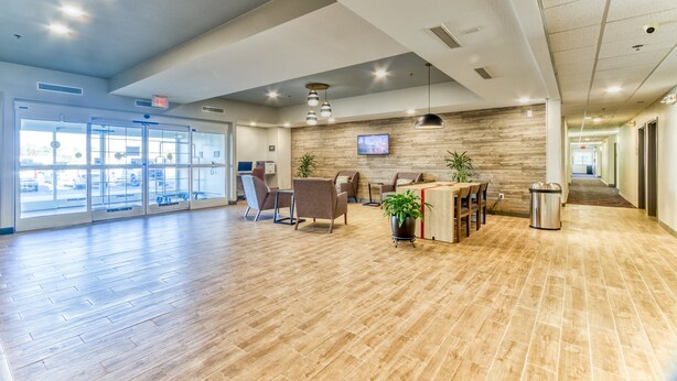 A spacious lobby with wooden flooring, seating areas, a reception desk, and a television mounted on the wall.