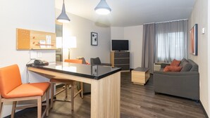 A modern living room with a wooden dining table, orange chairs, a grey sofa, and a TV on a wooden cabinet.
