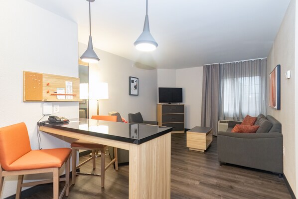 Een moderne woonkamer met een houten eettafel, oranje stoelen, een grijze bank en een televisie op een houten kast.