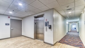 Un couloir d’hôtel avec un ascenseur, une porte portant l’inscription « Local électrique » et un tapis à motifs.