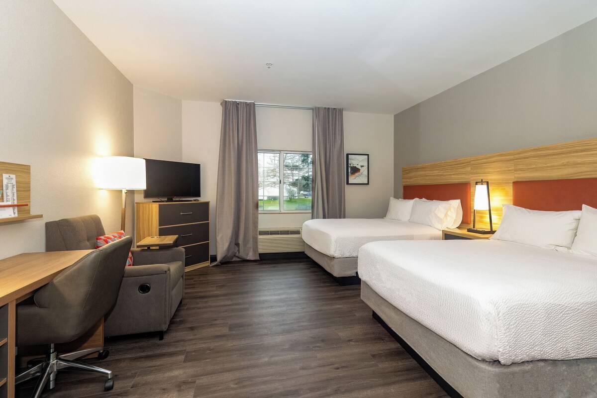 Een hotelkamer met een bureau, twee bedden, een televisie en een raam met gordijnen.