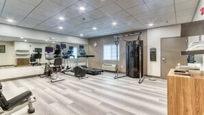 Une salle de sport équipée de divers appareils d’exercice, un comptoir d’accueil et un grand miroir mural.