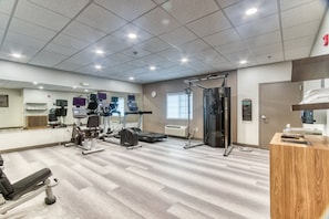 Een sportschool met diverse fitnessapparaten, een receptiebalie en een grote spiegel aan de muur.