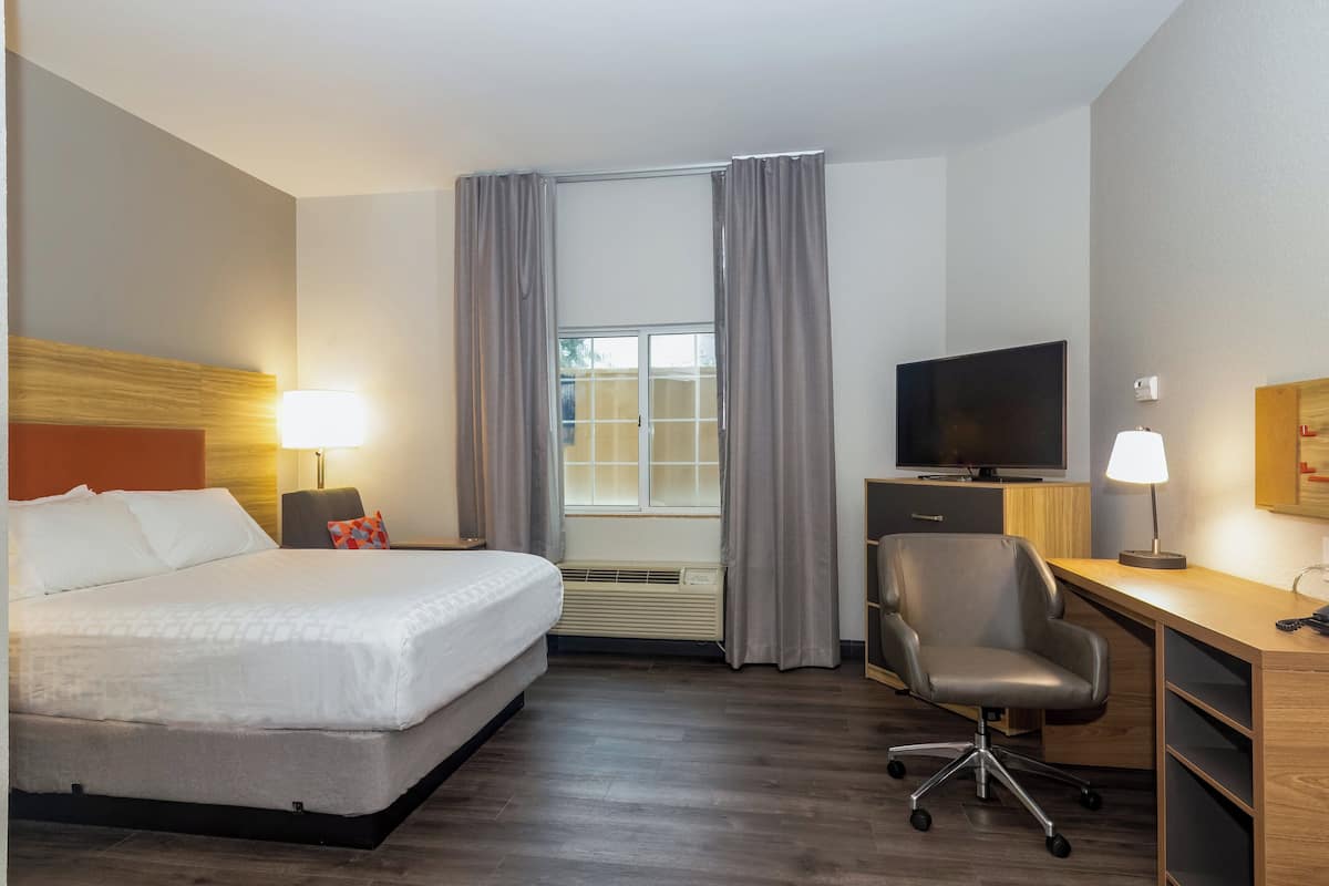 Une chambre d’hôtel équipée d’un lit, d’un bureau, d’une chaise, d’une télévision et d’une fenêtre avec des rideaux.