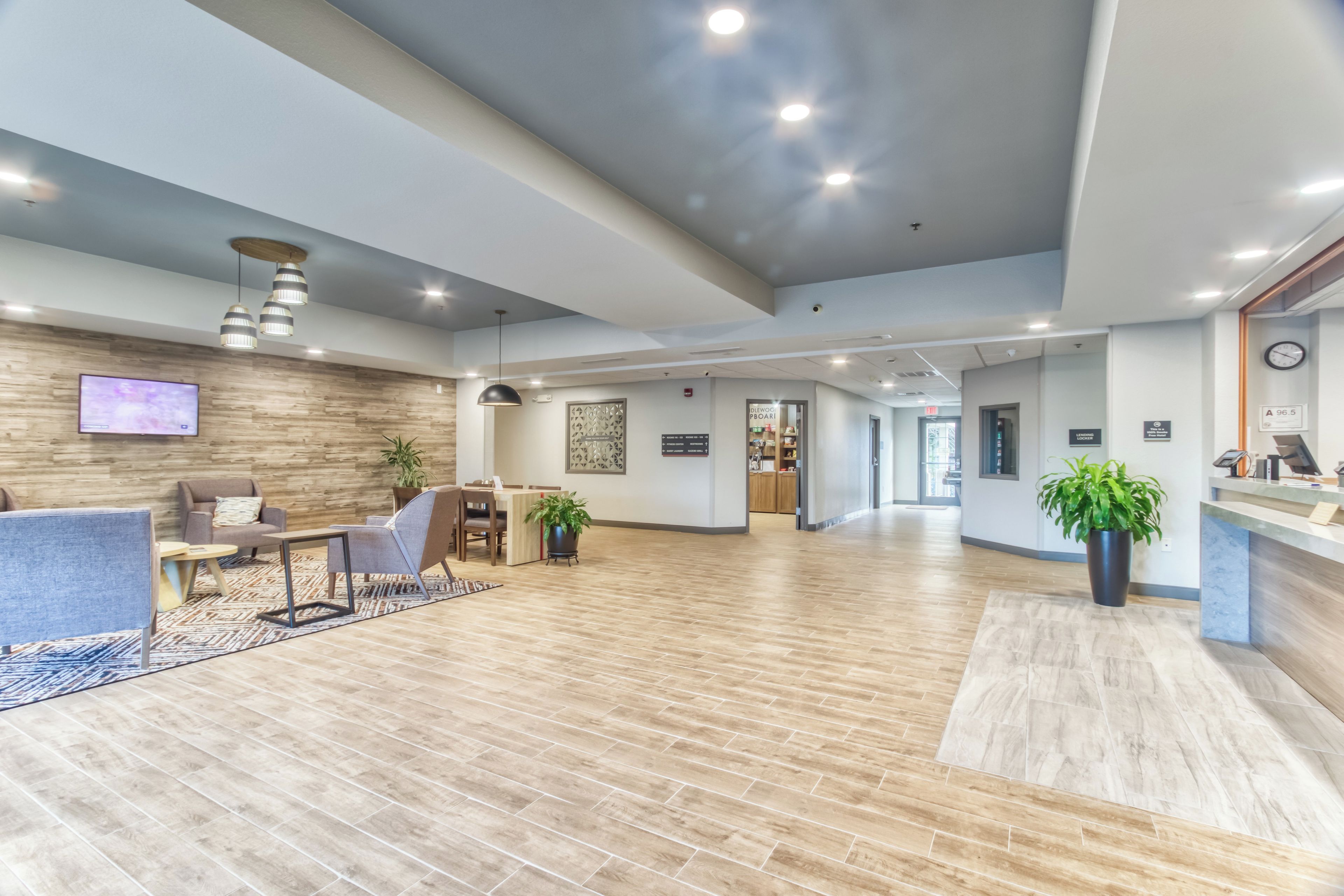 A spacious lobby with a reception desk, seating area, and a wooden floor.