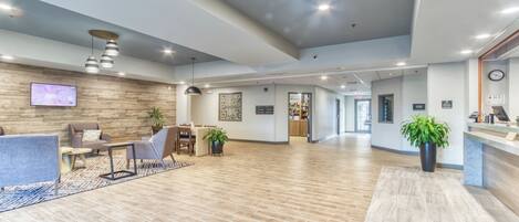 A spacious lobby with a reception desk, seating area, and a wooden floor.