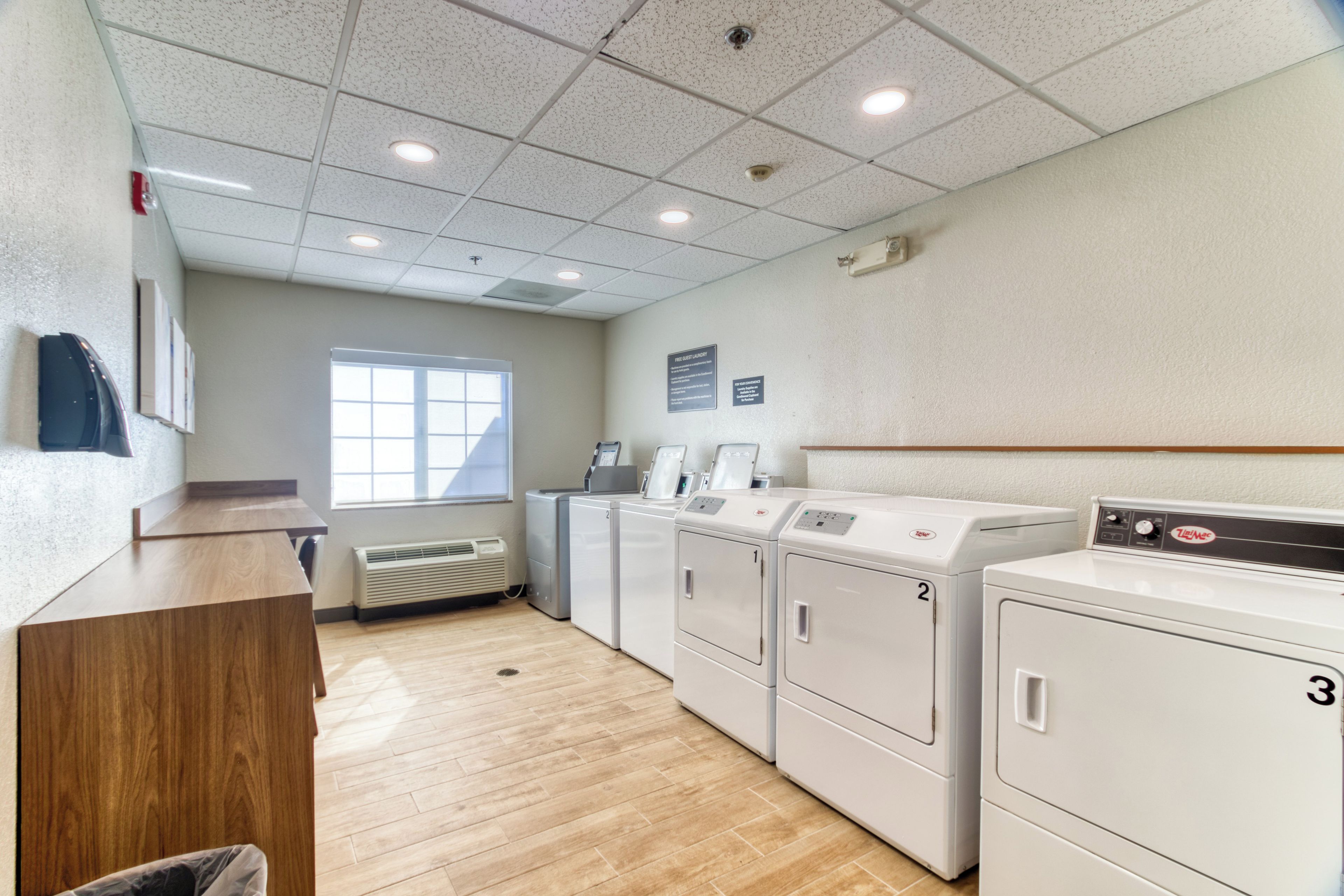 A laundry facility with multiple washing machines, a drying machine, a water heater, and a window providing natural light.
