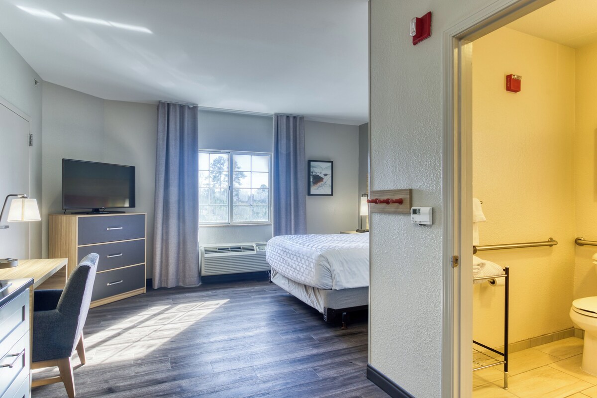Een hotelkamer met een bed, een bureau met stoel, een televisie, een raam met gordijnen en een badkamer.