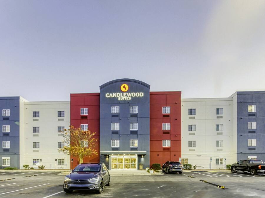 Un hotel con un letrero llamativo de 'Candlewood Suites', varios pisos y un estacionamiento con varios coches.