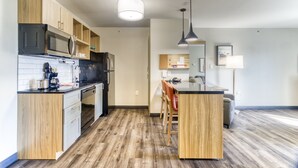 A modern kitchen with wooden cabinets, a microwave, and a refrigerator. There is a dining area with a table and chairs.