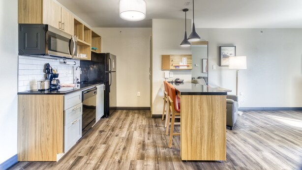 Une cuisine moderne avec des meubles en bois, un four à micro-ondes et un réfrigérateur. Un coin repas est aménagé avec une table et des chaises.