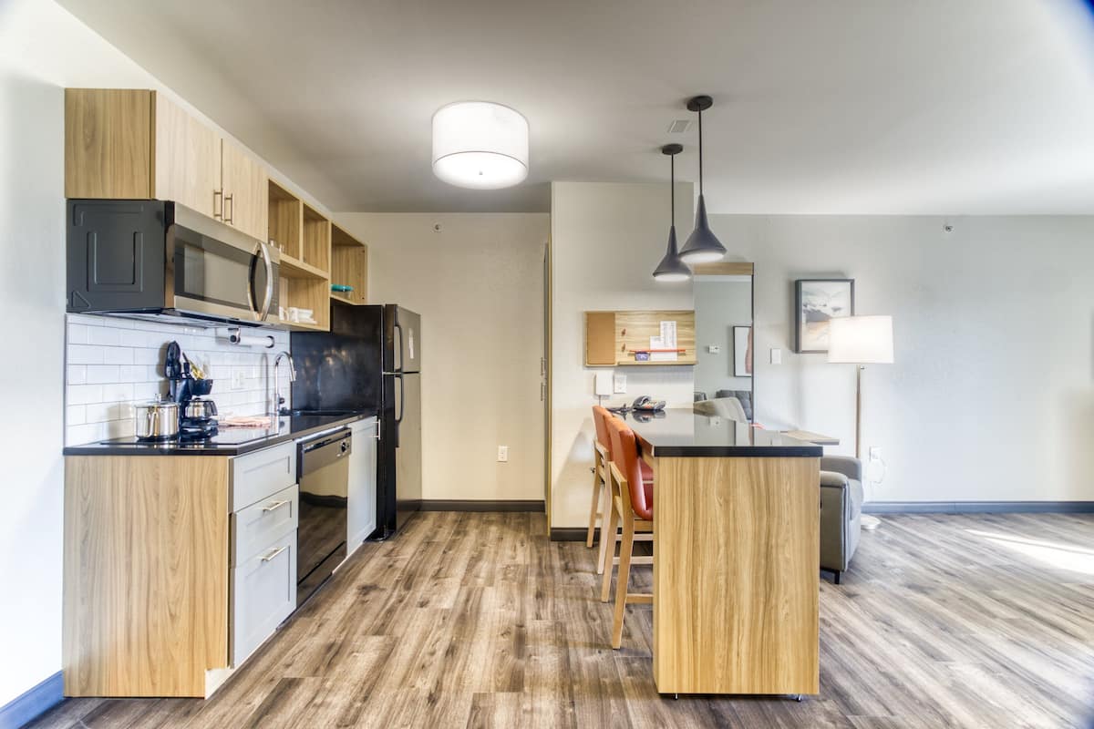 Une cuisine moderne avec des meubles en bois, un four à micro-ondes et un réfrigérateur. Un coin repas est aménagé avec une table et des chaises.