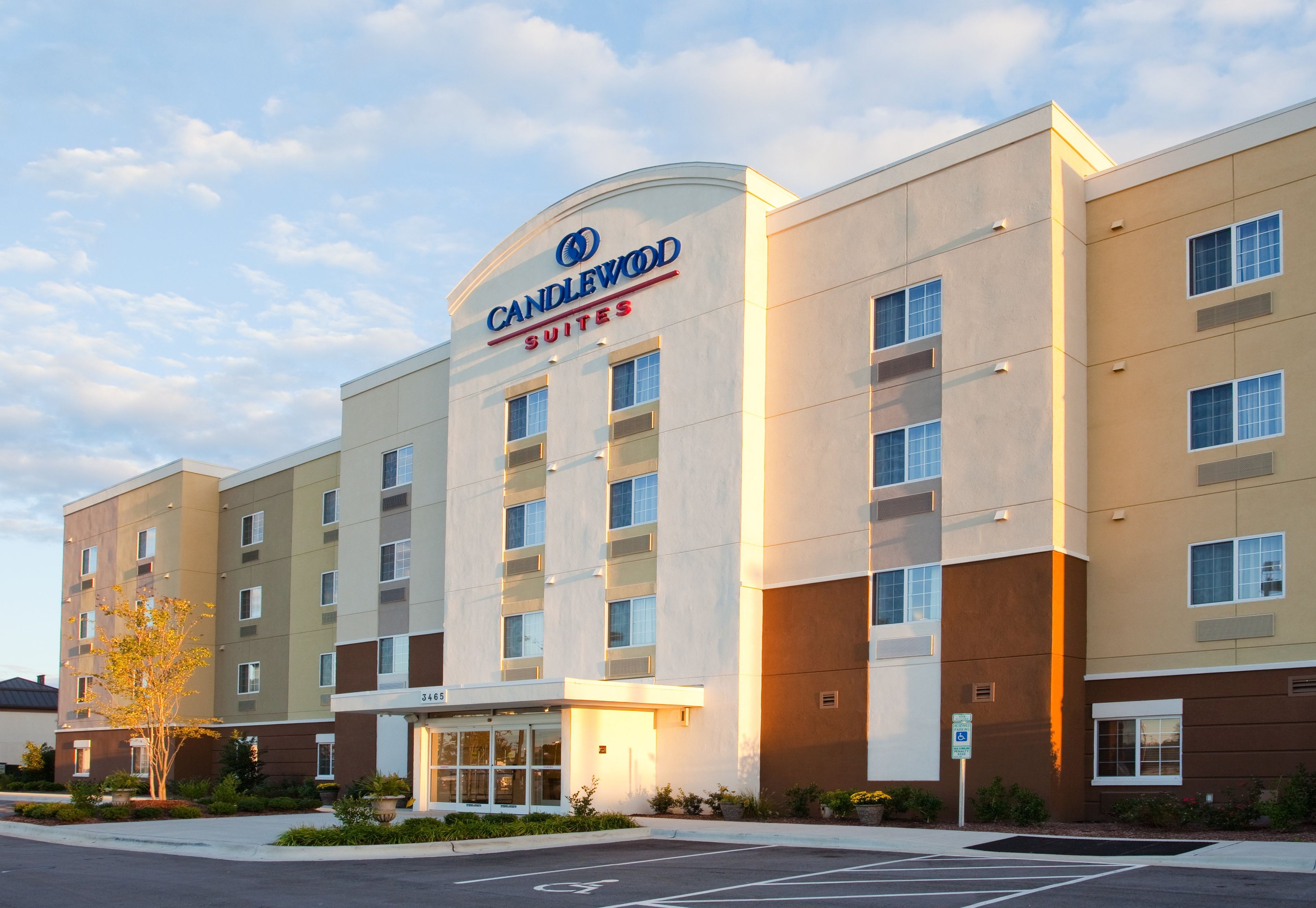 A multi-story hotel with a prominent 'Candlewood Suites' sign, a parking lot, and a landscaped entrance area.