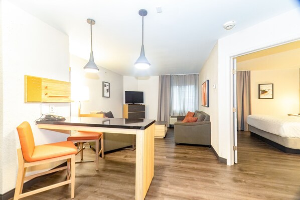 Een moderne hotelkamer met houten vloer, een zithoek met tafel en stoelen, een bank, een bed en een televisie.