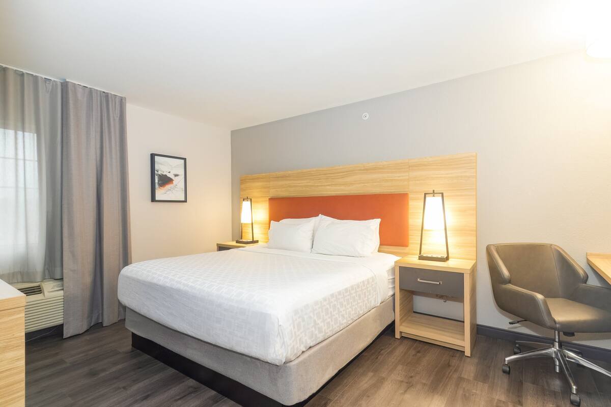 Une chambre d’hôtel avec un grand lit, un bureau avec une chaise, une table de chevet avec une lampe et un tableau au mur.