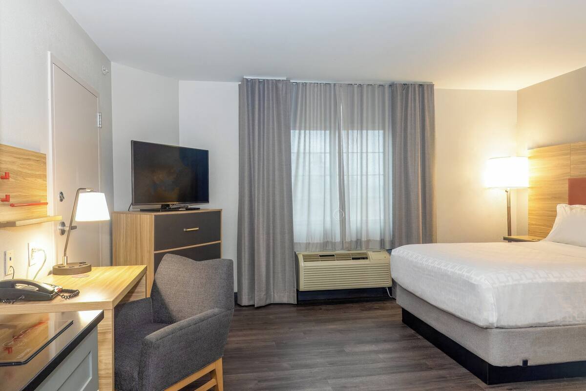 Une chambre d’hôtel comprenant un lit, un bureau avec un téléphone, une chaise, une télévision et une fenêtre avec des rideaux.