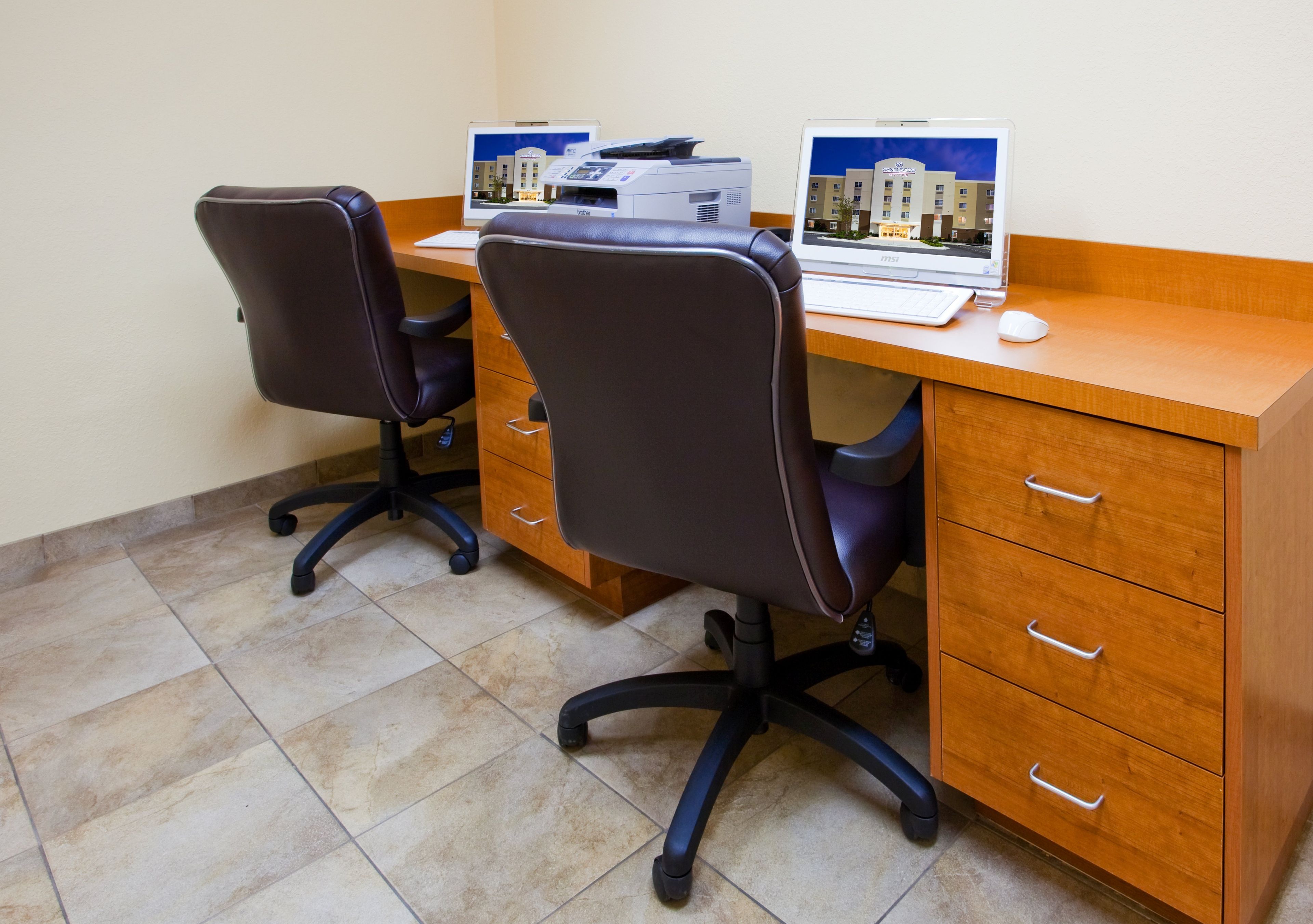A workspace with two office chairs, a wooden desk, a printer, and a computer monitor.