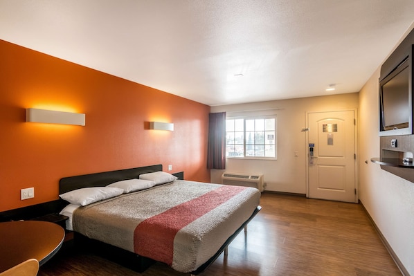 Une chambre d’hôtel avec un lit, un bureau, une chaise, une télévision et une fenêtre avec des rideaux.