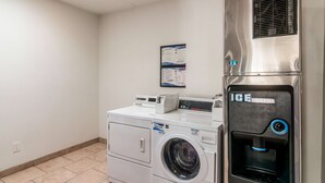 A laundry area with a front-loading washer and dryer, an ice dispenser, and a wall-mounted information board. - Motel 6 Bell Gardens, CA - Los Angeles (Bell Gardens)
